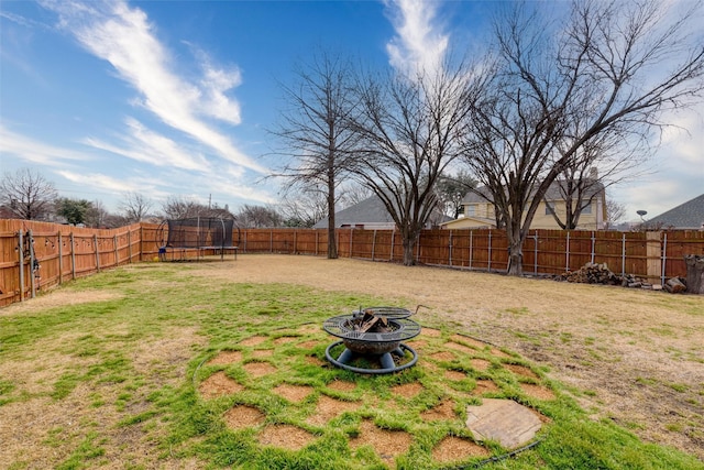 view of yard featuring a trampoline, a fenced backyard, and a fire pit