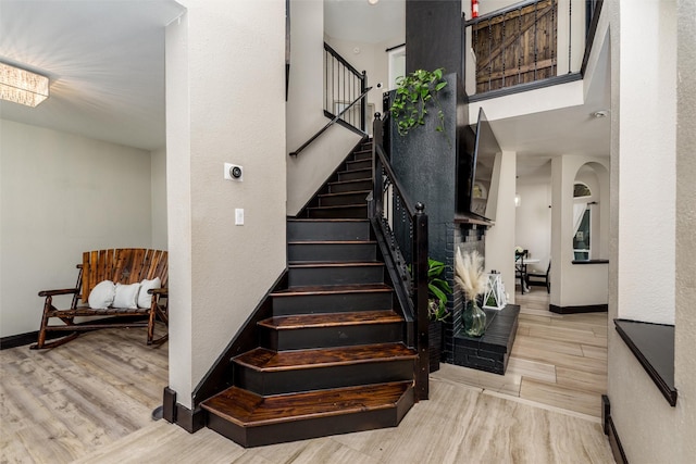 stairs with arched walkways, baseboards, and wood finished floors