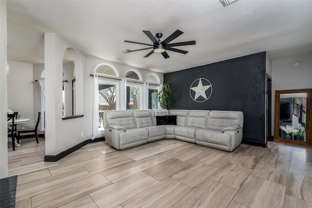 living area with a ceiling fan, wood finish floors, an accent wall, and baseboards