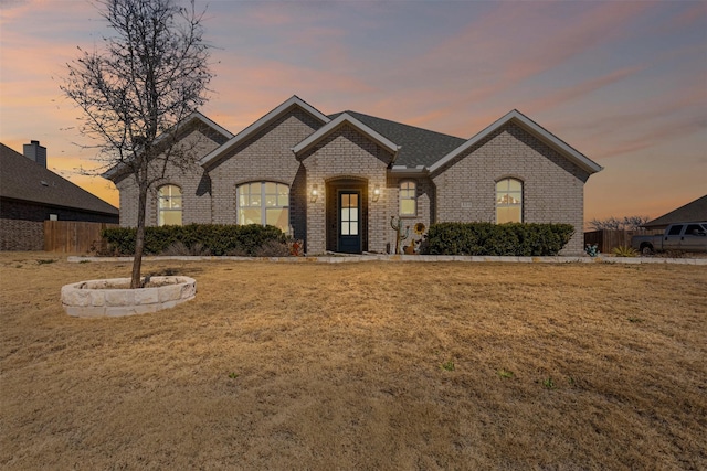 french provincial home featuring brick siding, a yard, and fence