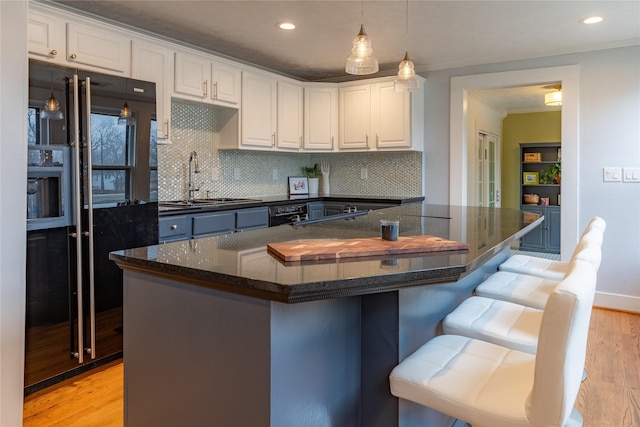 kitchen featuring pendant lighting, light wood-style floors, white cabinetry, a sink, and a kitchen breakfast bar