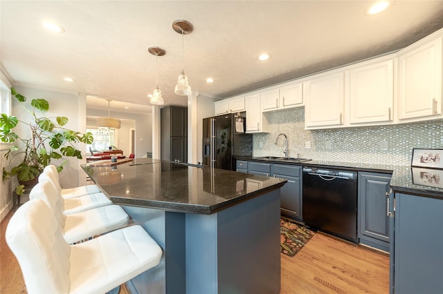 kitchen featuring decorative light fixtures, white cabinets, a kitchen island, a sink, and black appliances