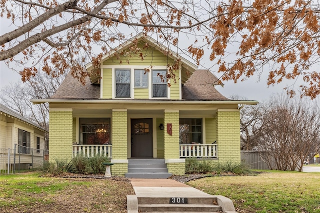 view of front facade featuring covered porch, brick siding, a front lawn, and roof with shingles