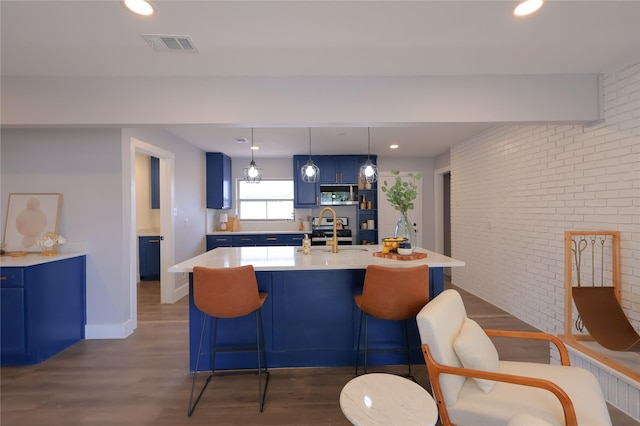 kitchen featuring a center island with sink, brick wall, hanging light fixtures, blue cabinets, and light countertops