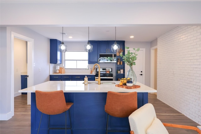 kitchen with blue cabinetry, light countertops, a kitchen island with sink, a sink, and brick wall