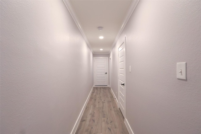 hallway featuring baseboards, a textured wall, light wood-style flooring, and crown molding