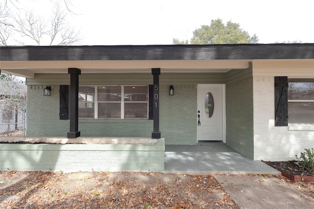 view of exterior entry with covered porch and brick siding