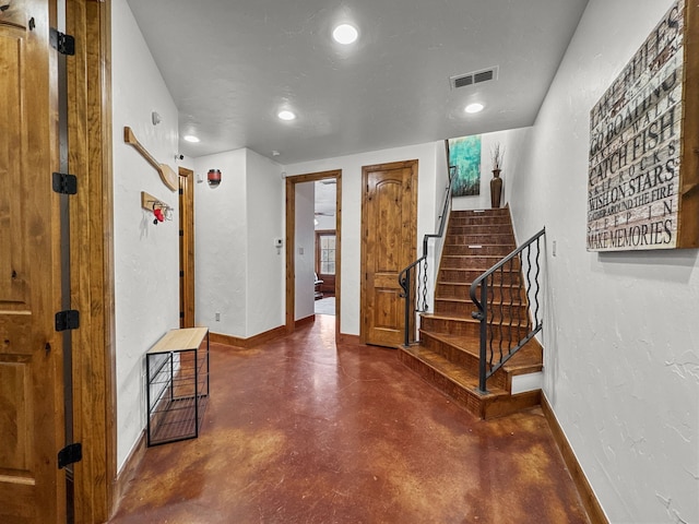 foyer featuring visible vents, a textured wall, stairway, finished concrete floors, and baseboards