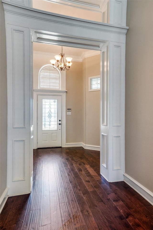 entrance foyer with baseboards, a notable chandelier, ornamental molding, and dark wood-type flooring