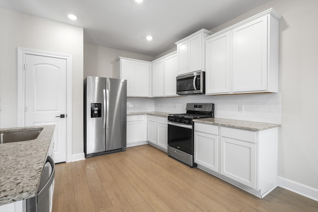 kitchen with light stone countertops, white cabinetry, stainless steel appliances, and light wood-style floors