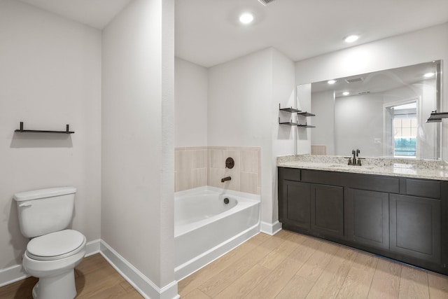 bathroom with a garden tub, toilet, vanity, wood finished floors, and baseboards