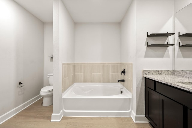 bathroom with toilet, wood finished floors, vanity, baseboards, and a bath