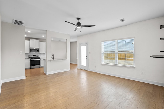 unfurnished living room featuring a ceiling fan, light wood-type flooring, visible vents, and a sink