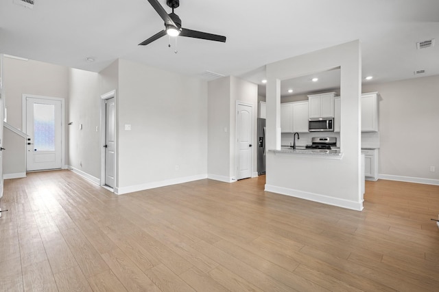 unfurnished living room featuring ceiling fan, a sink, visible vents, baseboards, and light wood finished floors