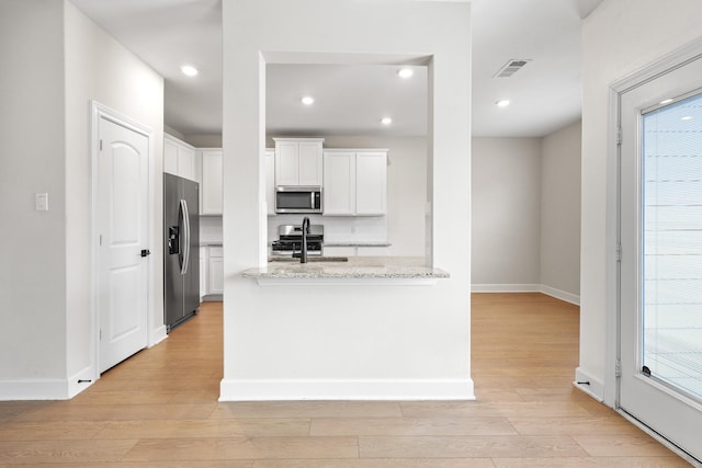 kitchen featuring light wood finished floors, visible vents, white cabinets, light stone counters, and stainless steel appliances