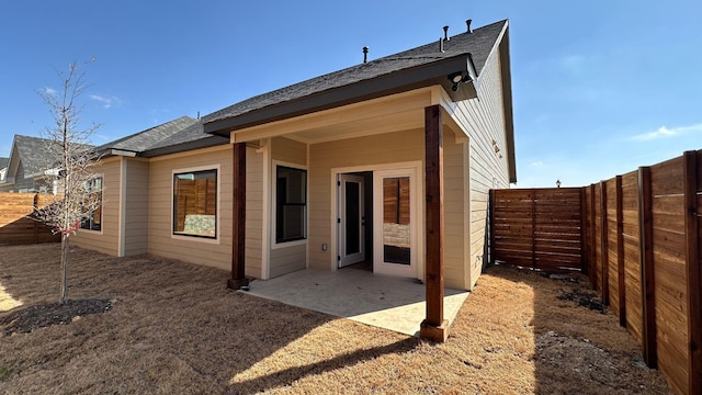 rear view of property featuring a patio area, a fenced backyard, and a shingled roof