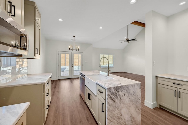 kitchen with light stone counters, stainless steel appliances, cream cabinetry, an island with sink, and pendant lighting