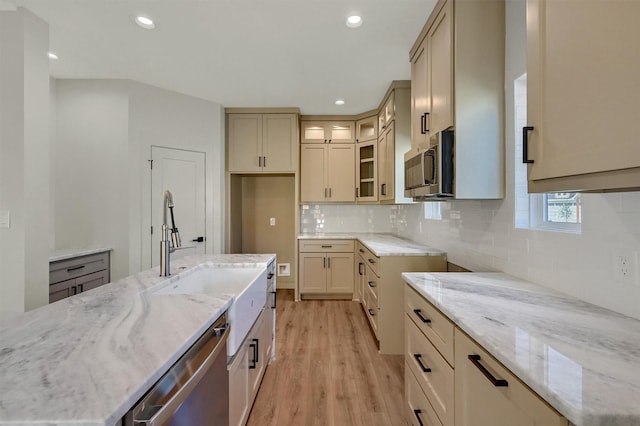 kitchen featuring stainless steel appliances, light stone counters, light wood-type flooring, and glass insert cabinets