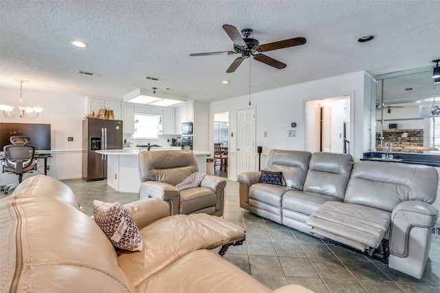 living area with ceiling fan with notable chandelier, a textured ceiling, tile patterned flooring, and visible vents