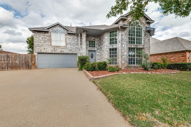 traditional home with driveway, a garage, fence, a front lawn, and brick siding