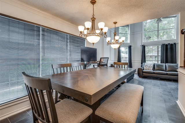 dining area featuring dark tile patterned flooring, ornamental molding, an inviting chandelier, a textured ceiling, and a decorative wall