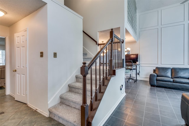 stairs with an inviting chandelier, baseboards, a decorative wall, and tile patterned floors