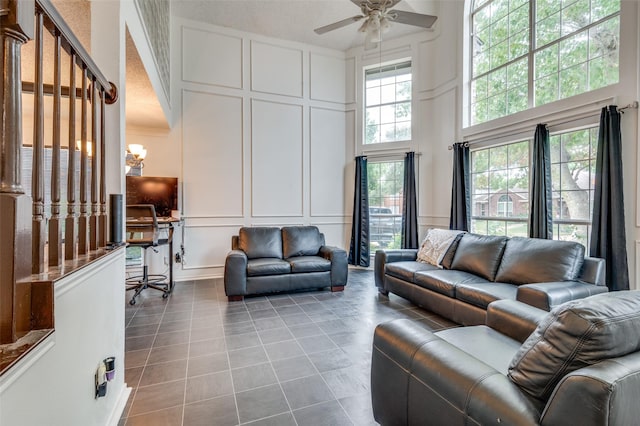 living area with ceiling fan with notable chandelier, a decorative wall, a towering ceiling, and light tile patterned floors