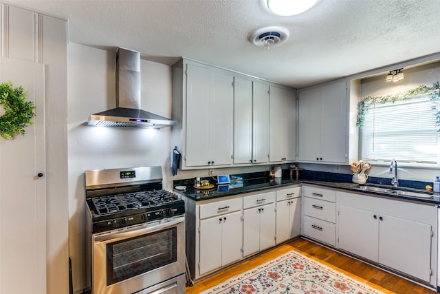 kitchen with light wood-style flooring, a sink, visible vents, wall chimney exhaust hood, and gas stove