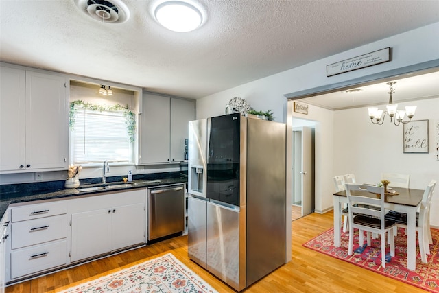 kitchen featuring light wood finished floors, dark countertops, hanging light fixtures, stainless steel appliances, and a sink