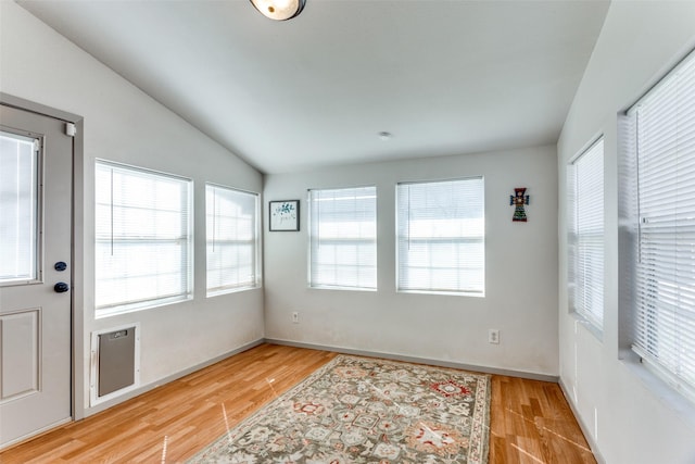 empty room with lofted ceiling, light wood-style floors, plenty of natural light, and baseboards