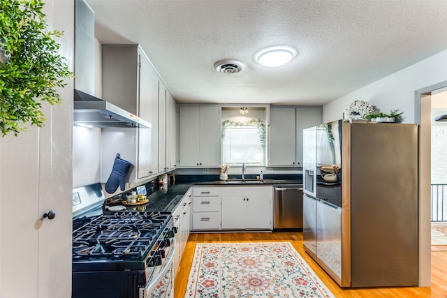 kitchen with visible vents, dark countertops, wall chimney exhaust hood, appliances with stainless steel finishes, and light wood-style floors