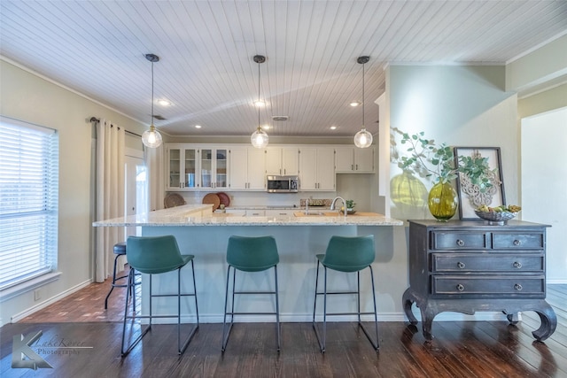 kitchen featuring dark wood finished floors, glass insert cabinets, stainless steel microwave, decorative light fixtures, and white cabinetry