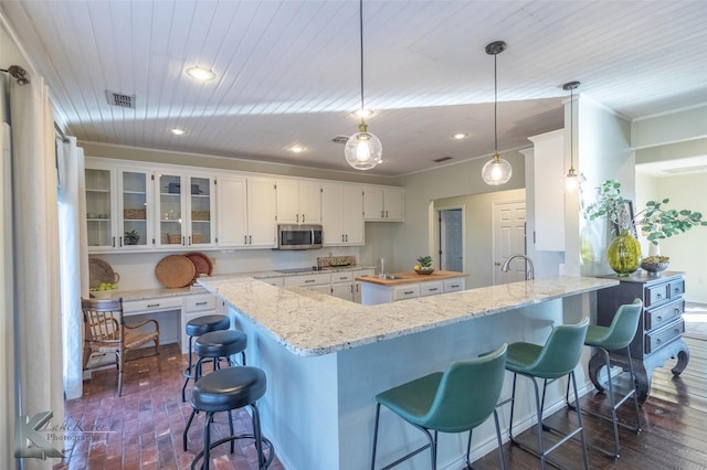 kitchen featuring a kitchen island, white cabinetry, hanging light fixtures, stainless steel microwave, and glass insert cabinets