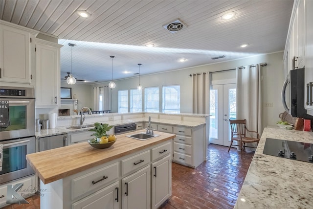 kitchen featuring white cabinets, a kitchen island with sink, stainless steel appliances, wooden counters, and a sink