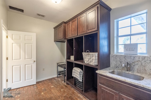 interior space with baseboards, visible vents, a sink, brick floor, and backsplash