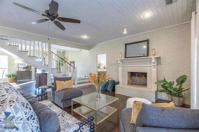 living room with brick wall, stairs, a fireplace, and wood finished floors