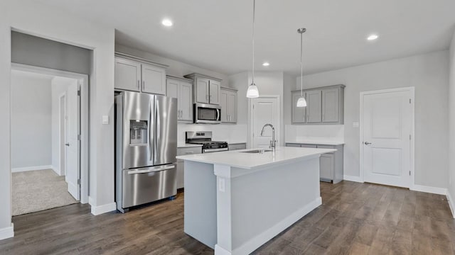 kitchen with stainless steel appliances, light countertops, gray cabinetry, a sink, and an island with sink