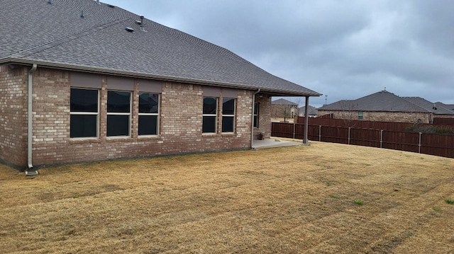 back of house with a yard, brick siding, fence, and roof with shingles