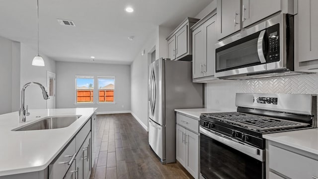 kitchen with tasteful backsplash, stainless steel appliances, light countertops, pendant lighting, and a sink