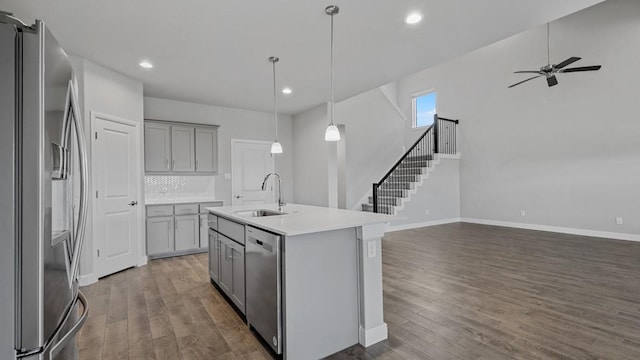 kitchen featuring a center island with sink, gray cabinets, stainless steel appliances, light countertops, and a sink