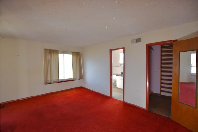 carpeted spare room featuring baseboards, visible vents, and a textured ceiling