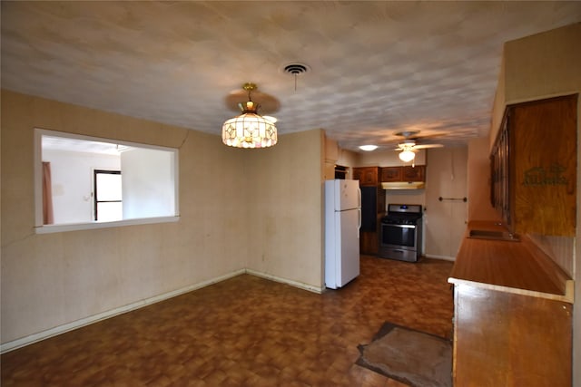 kitchen featuring under cabinet range hood, a sink, visible vents, stainless steel range with gas cooktop, and freestanding refrigerator