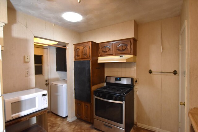 kitchen with stainless steel gas range oven, white microwave, under cabinet range hood, brown cabinets, and tasteful backsplash