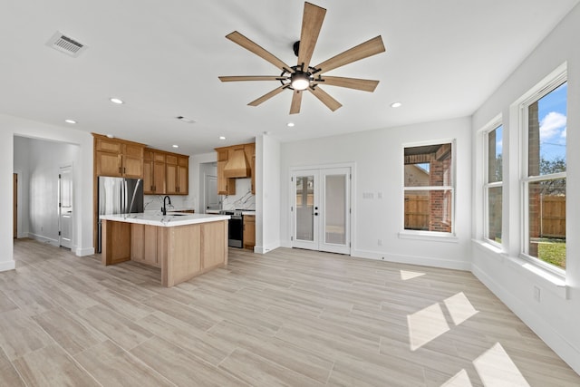 kitchen with stainless steel appliances, a sink, visible vents, brown cabinets, and a center island with sink