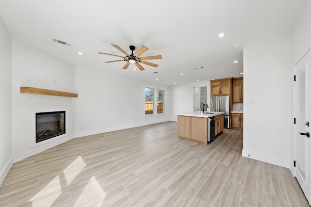 kitchen with open floor plan, a kitchen island with sink, light countertops, and visible vents