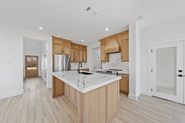 kitchen with visible vents, a kitchen island with sink, custom exhaust hood, stainless steel appliances, and a sink