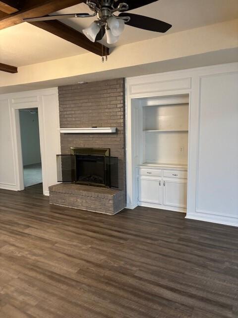 unfurnished living room featuring dark wood-type flooring, a brick fireplace, and beam ceiling