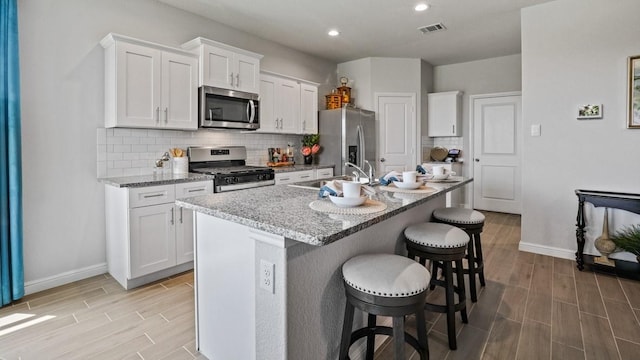 kitchen with a kitchen breakfast bar, stainless steel appliances, a center island with sink, and white cabinets