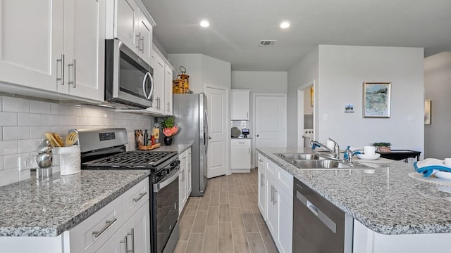 kitchen with appliances with stainless steel finishes, a sink, a kitchen island with sink, and white cabinets