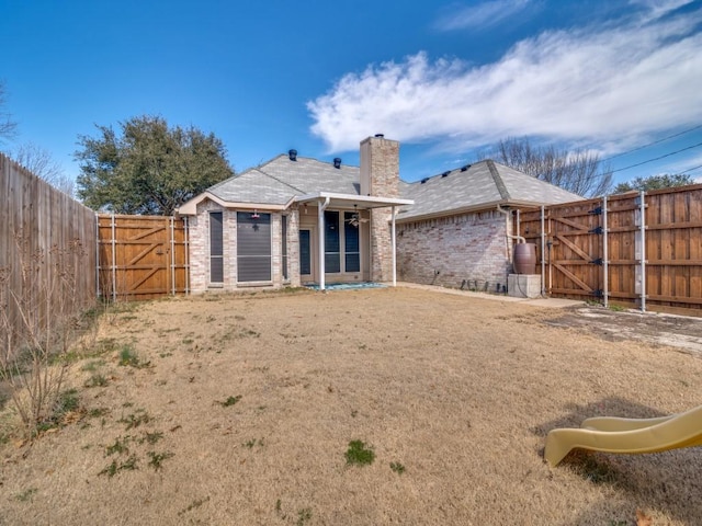 back of house with a gate, brick siding, fence, and a chimney